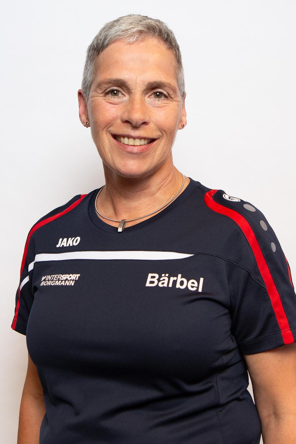 Porträt einer lächelnden Frau mit kurzer grauer Frisur, in einem Sporttrikot mit Aufdruck "Bärbel" und Logo.