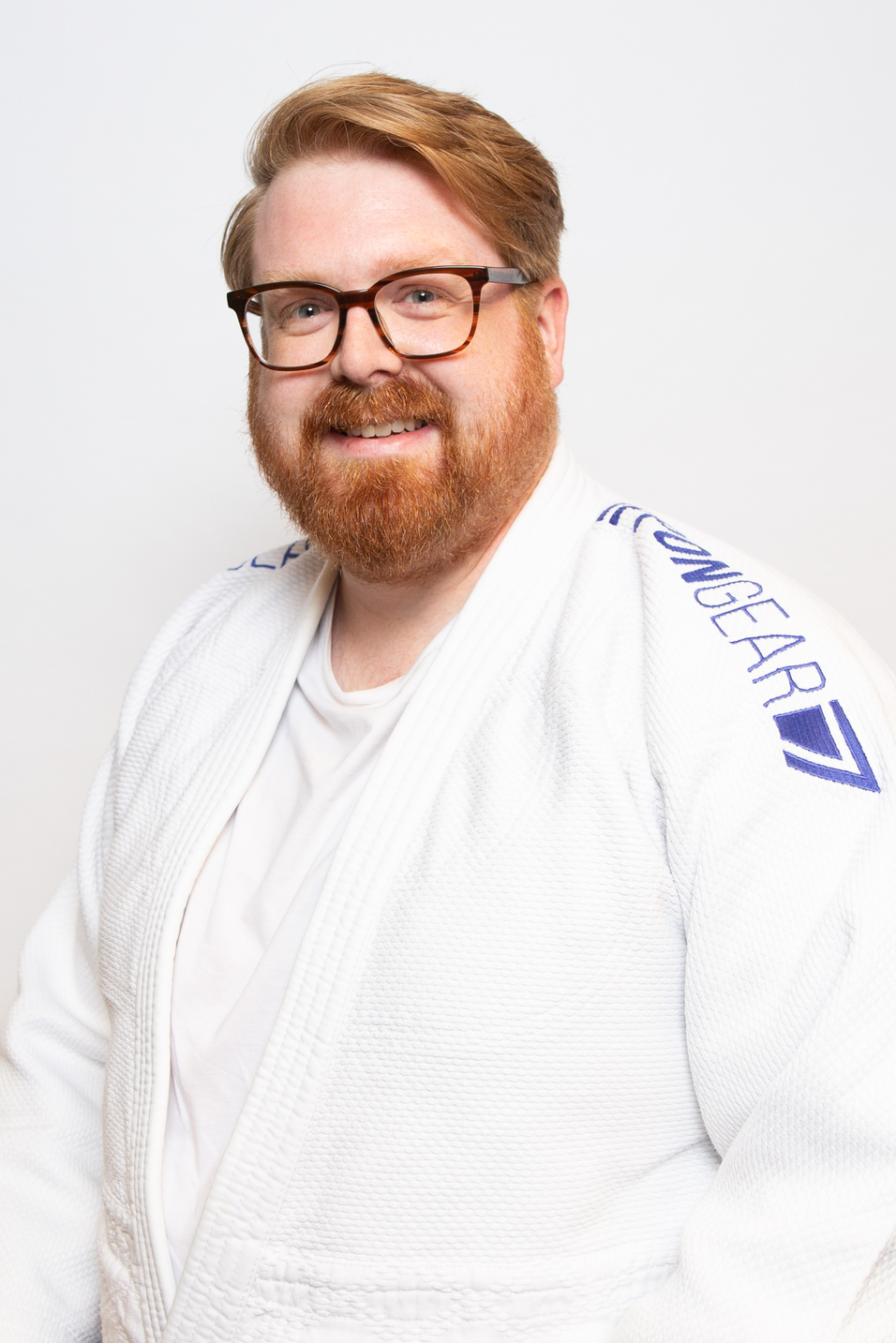 L&auml;chelnder Mann mit Brille tr&auml;gt einen wei&szlig;en Judogi und posiert vor einem neutralen Hintergrund.