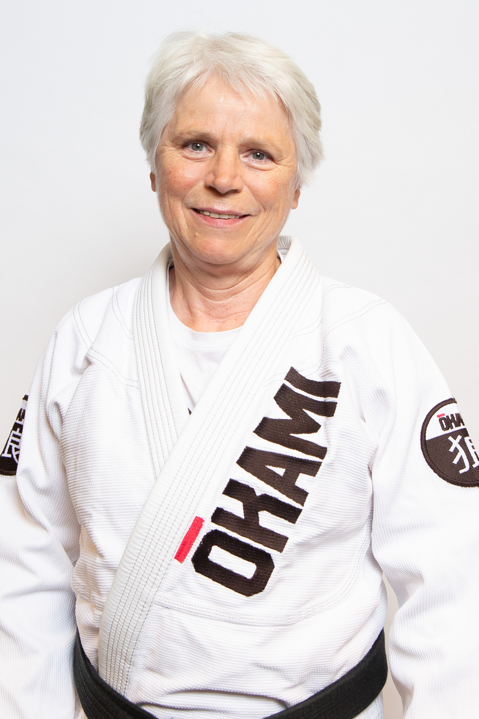 Portr&auml;t einer l&auml;chelnden Frau in einem wei&szlig;en Judoanzug mit schwarzem G&uuml;rtel vor wei&szlig;em Hintergrund.