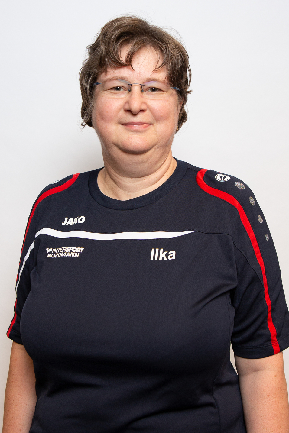 Portrait einer Frau in einem dunklen Sportshirt mit roten und grauen Akzenten, auf einem neutralen Hintergrund.