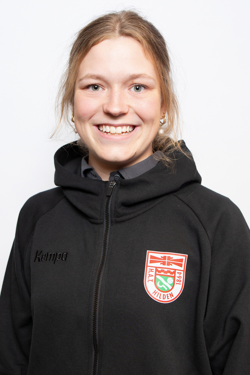 Portrait einer l&auml;chelnden jungen Frau in schwarzer Kapuzensweatjacke mit Kempa-Logo und Vereinswappen von Hilden.