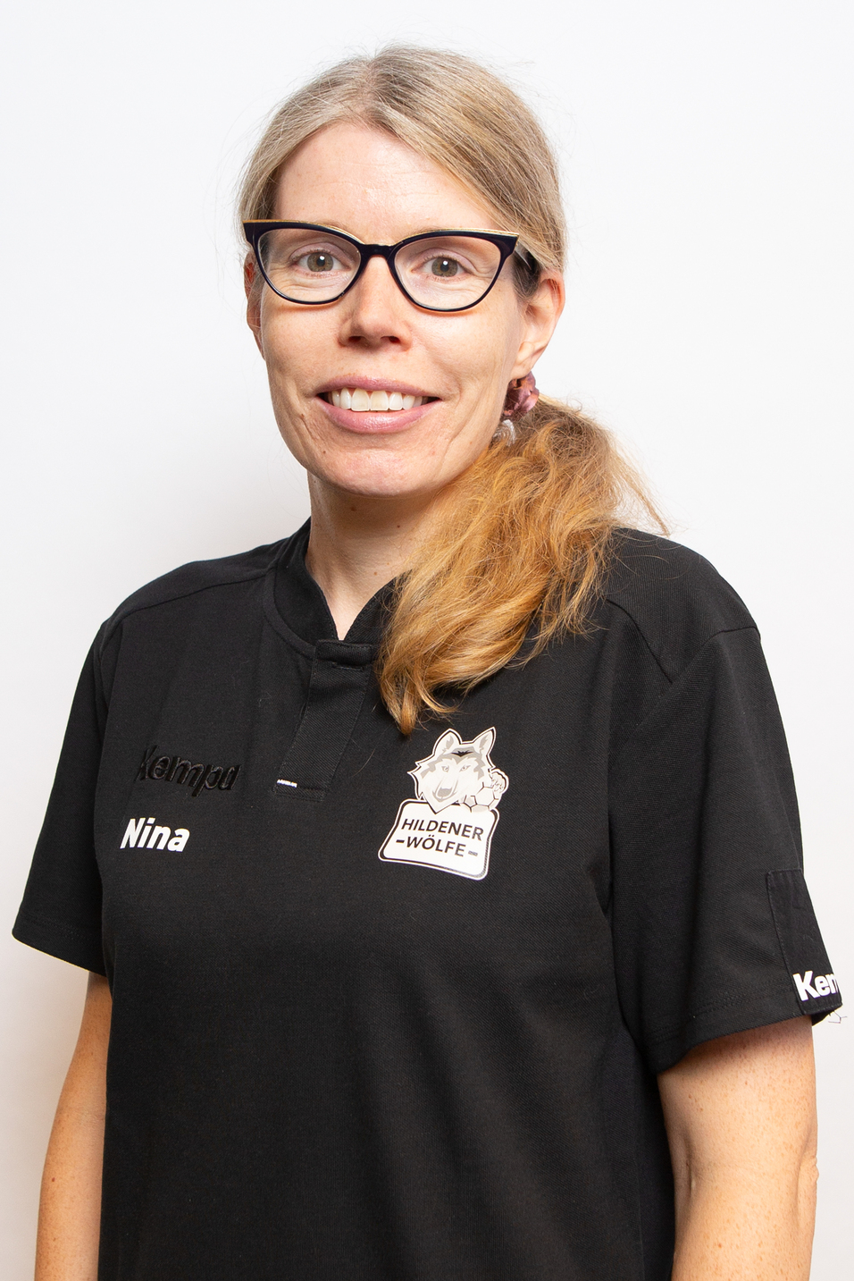 Portr&auml;t einer Frau mit langen, blonden Haaren, die ein schwarzes Sporttrikot mit Logo und Namen tr&auml;gt.