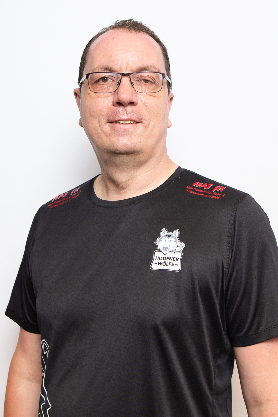 Portrait eines Mannes mit Brille in einem schwarzen T-Shirt mit dem Logo der Hildener W&ouml;lfe vor wei&szlig;em Hintergrund.