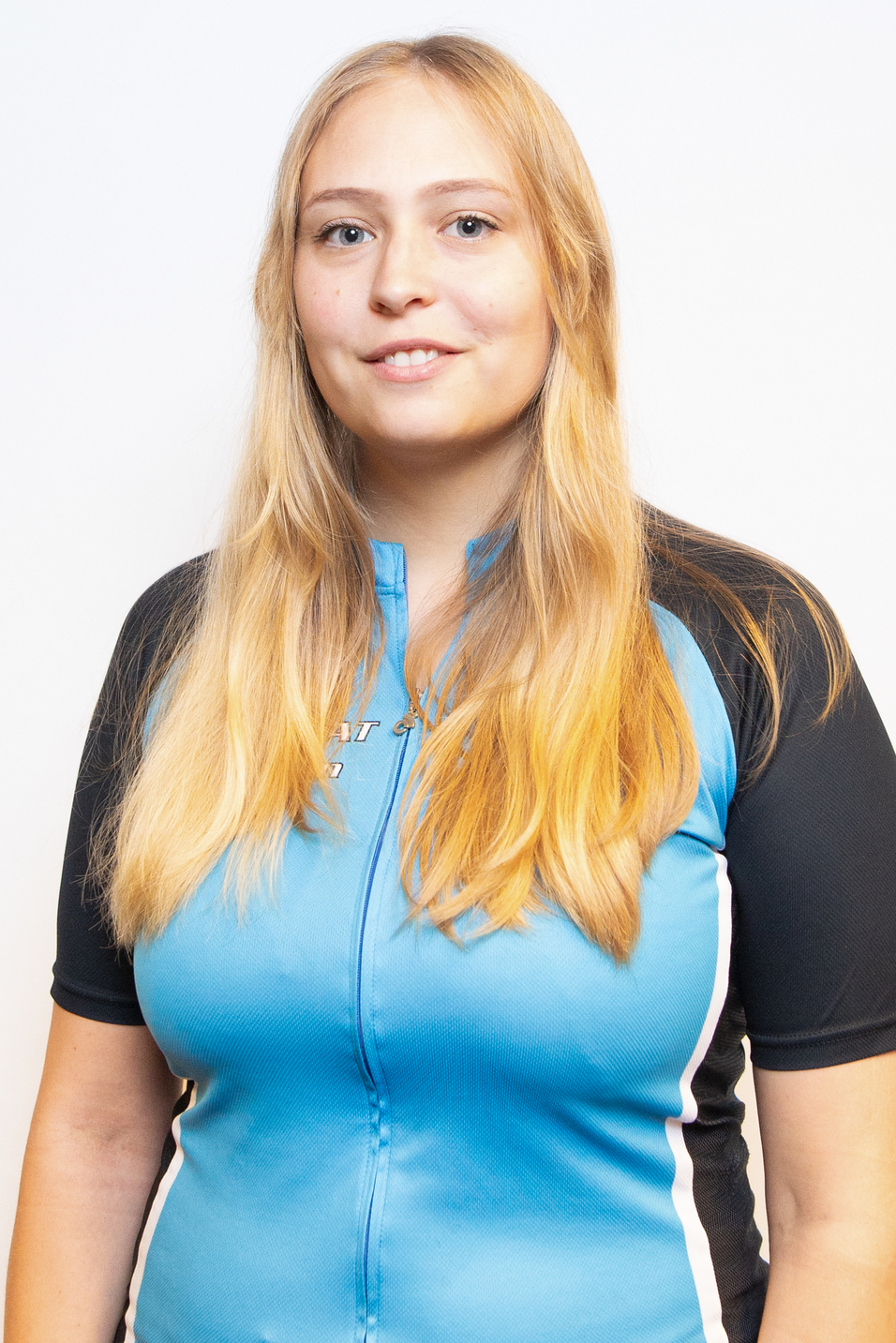 Portr&auml;t einer Frau mit langen blonden Haaren in einem blauen Radtrikot, freundlich l&auml;chelnd vor neutralem Hintergrund.