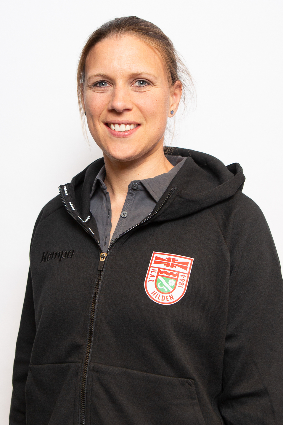 Portrait einer l&auml;chelnden Frau in einem schwarzen Hoodie mit Kappa-Logo und Vereinswappen von Hilden.