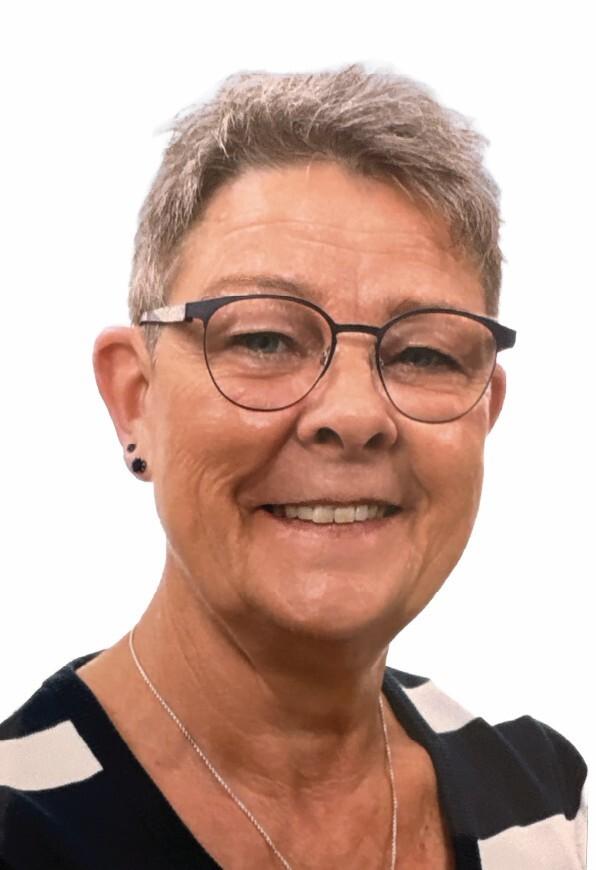 Porträt einer lächelnden Frau mit kurzen grauen Haaren und Brille, die ein gestreiftes Oberteil trägt.