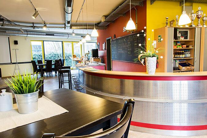 Innenansicht eines modernen Cafés mit einer Theke, Tischen und Stühlen, hellen Wänden und Pflanzen.