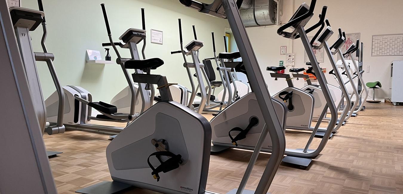 Moderne Fitnessgeräte in einem lichtdurchfluteten Raum, mit mehreren Fahrradergometern auf einem Holzfußboden.