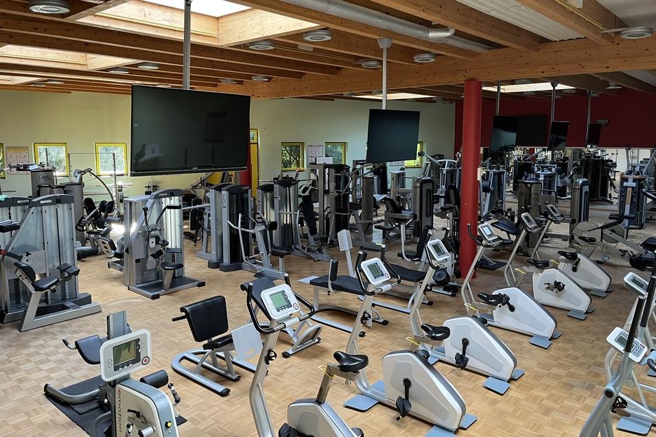 Fitnessstudio mit verschiedenen Trainingsgeräten, darunter Laufbänder und Krafttrainingsmaschinen, in einem hellen Raum.