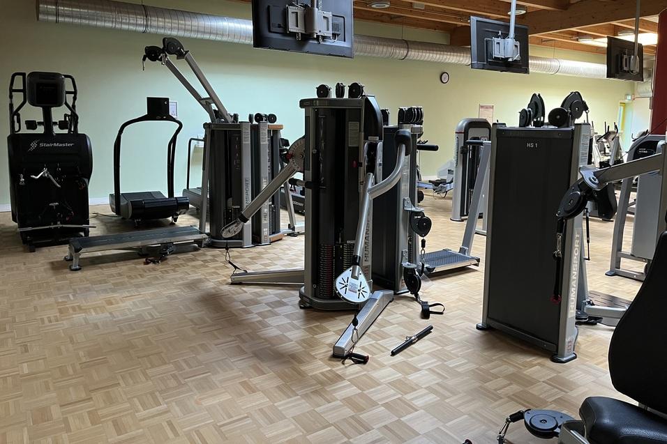 Moderne Fitnessgeräte im Innenraum eines Fitnessstudios mit Holzfußboden und mehreren Bildschirmmonitoren.