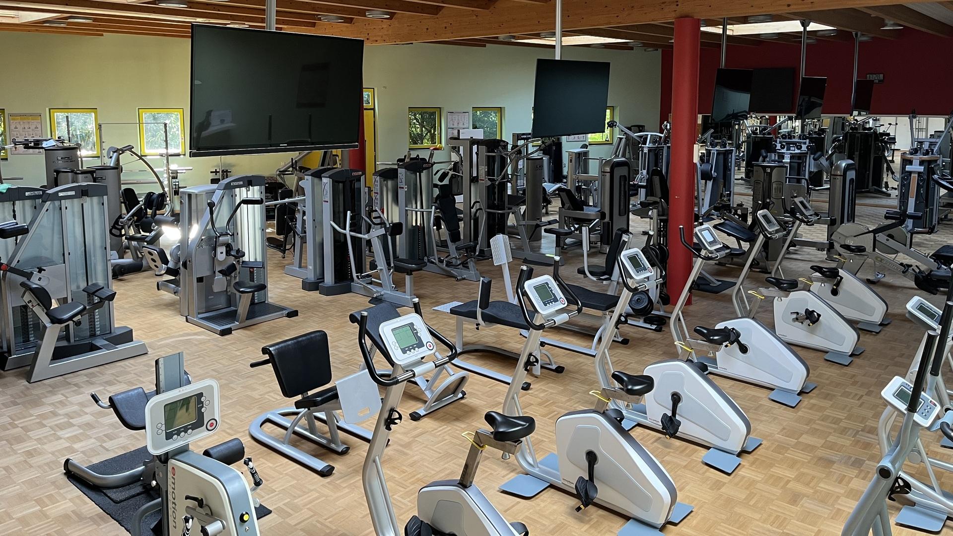 Fitnessstudio mit verschiedenen Trainingsger&auml;ten, darunter Laufb&auml;nder und Krafttrainingsmaschinen, in einem hellen Raum.