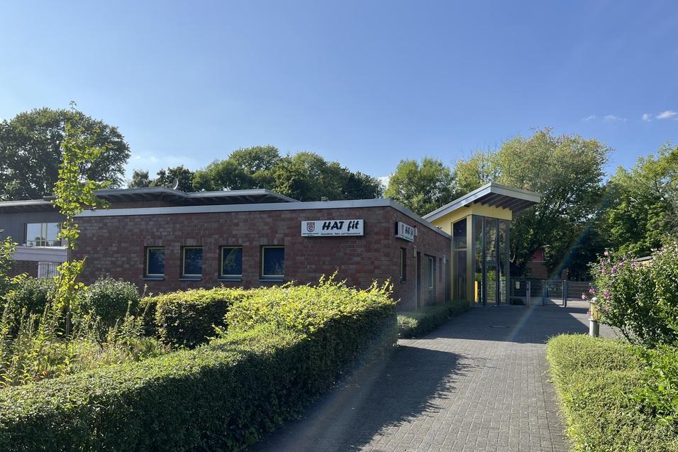 Eingang zu einem modernen Gebäude mit großen Fenstern, umgeben von grünen Pflanzen und einem gepflasterten Weg.