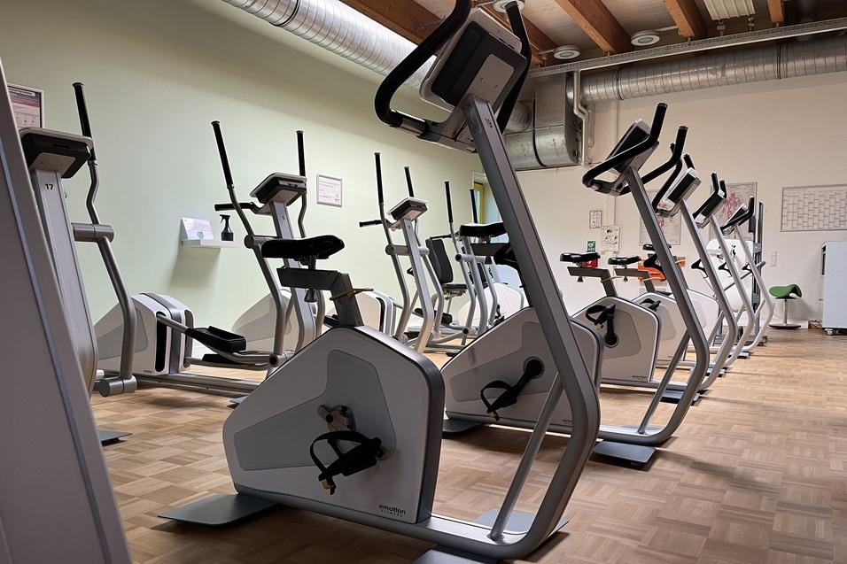 Moderne Fitnessgeräte in einem lichtdurchfluteten Raum, mit mehreren Fahrradergometern auf einem Holzfußboden.