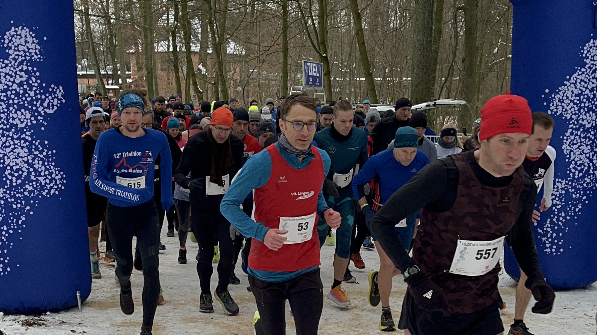 L&auml;ufer starten beim Hildener Winterlauf unter einem blauen Veranstaltungsbogen im verschneiten Wald.