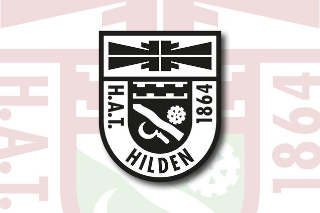 Wappen des H.A.T. Hilden mit Jahreszahl 1864 und verschiedenen Symbolen auf einem hellen Hintergrund.