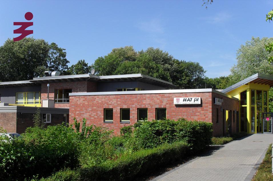 Gebäude mit roter Backsteinfassade, umliegendem Grün und gelbem Eingangsbereich. Beschilderung „HAT H“.