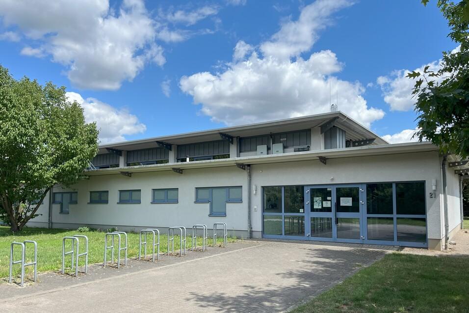 Modernes Geb&auml;ude mit gro&szlig;en Fenstern, Fahrradstellpl&auml;tzen und begr&uuml;nter Umgebung unter einem wolkigen Himmel.