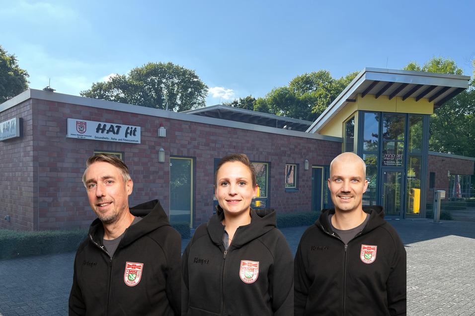 Drei Personen in sportlichen Hoodie-Shirts stehen vor einem modernen Fitnessstudio mit gelben Akzenten.
