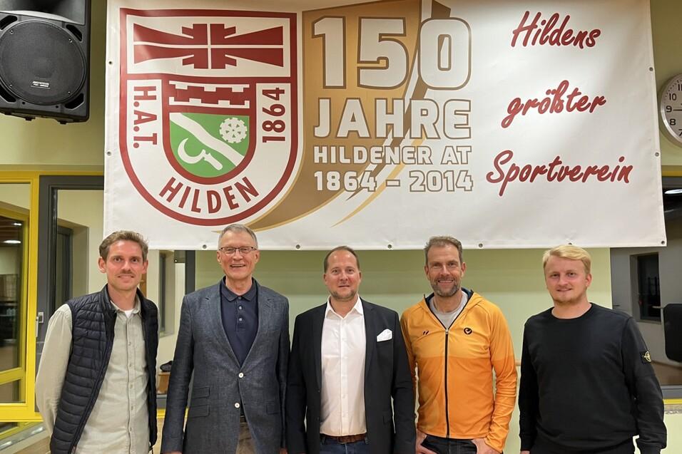 F&uuml;nf Personen stehen l&auml;chelnd vor einem Banner, das das 150-j&auml;hrige Jubil&auml;um des Sportvereins Hilden feiert.