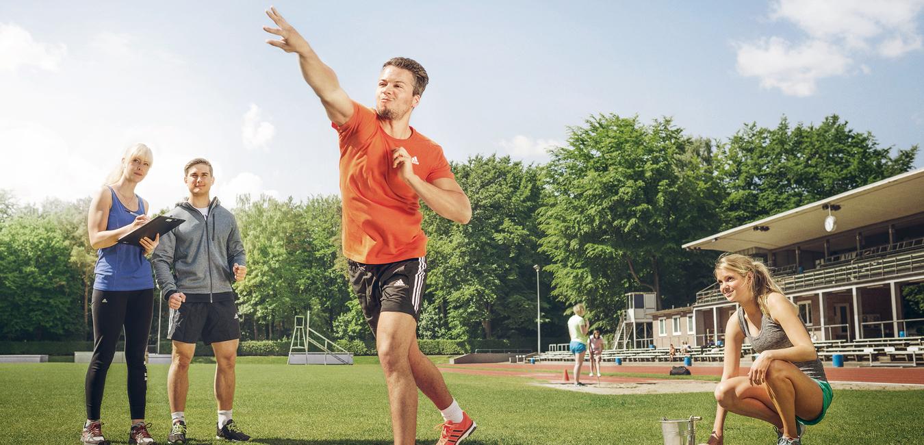 Ein Mann stößt eine Kugel im Stadion, drei Personen beobachten und messen daneben