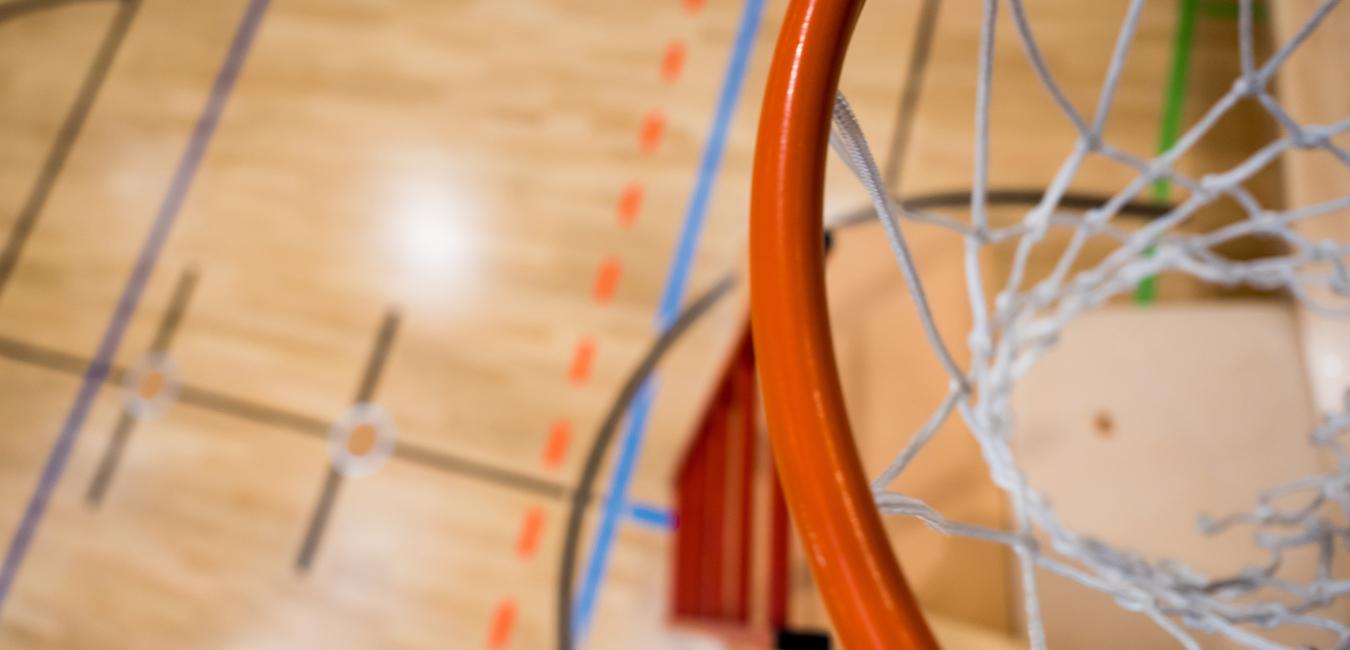 Nahaufnahme eines Basketballkorbs mit Netz über einem aufgezeichneten Basketballfeld aus Holz.