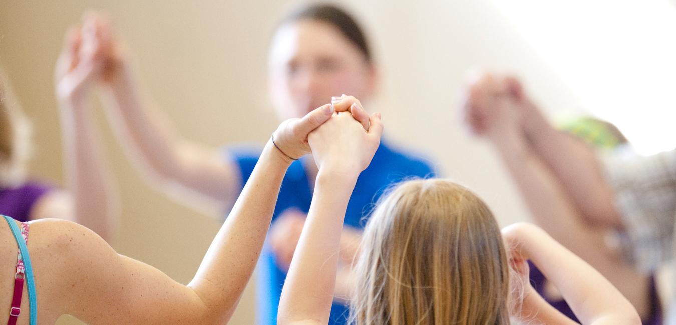 Gruppe von Kindern hält sich in einem gemeinsamen Kreis an den Händen, während sie in einer Sporthalle aktiv sind.