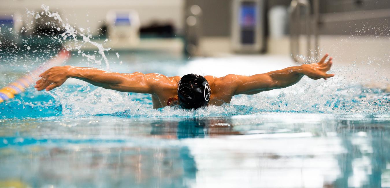 Schwimmer bei der Schmetterlingsbewegung im Wasser, Arme weit ausgebreitet, Spritzer um ihn herum.